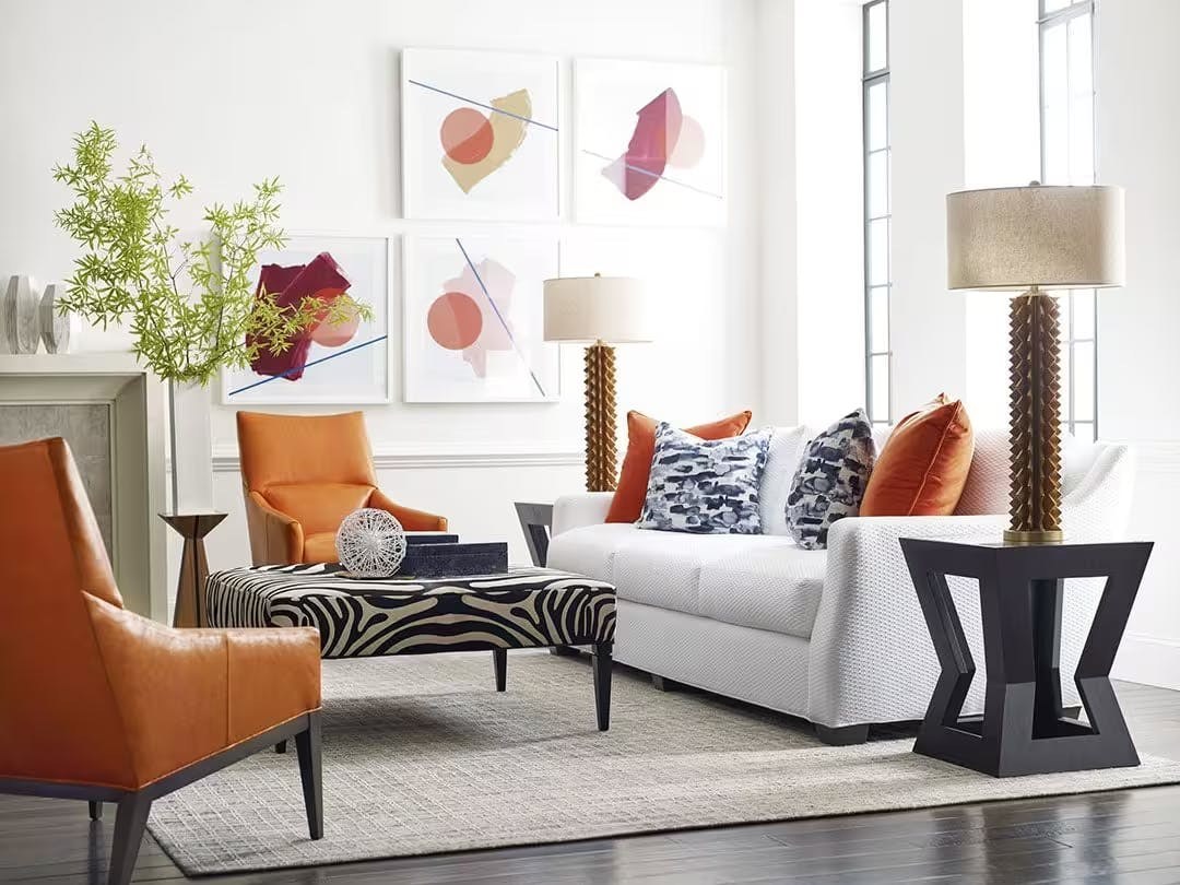 A styled room with a white sofa and orange accent chairs